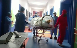 Imagen de un pasillo de un Centro Teletón. Hay 5 especialistas médicos vestidos con traje completo. Traen una camilla con un paciente, la camilla está cubierta por un domo de plástico, para proteger a los médicos del contagio por COVID-19