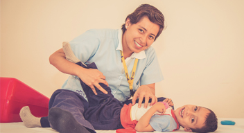 Imagen de niño con su terapeuta físico. La terapeuta está realizando estiramientos en la pierna del niño.