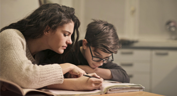 Fotografía de dos jóvenes, un hombre y una mujer, haciendo tarea en una misma libreta.