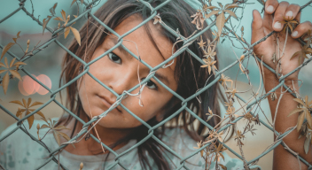 Niña en situación de pobreza mira a la cámara detrás de una reja de alambre. Foto por namo deet para Pexels