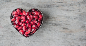 Fotografía de un plato con forma de corazón, lleno de granos de granada, sobre una mesa gris. Foto por Jessica Lewis para Pexels