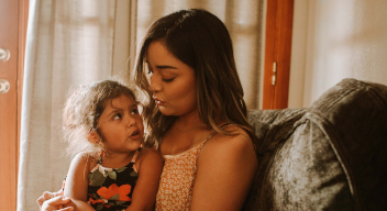 Fotografía de madre e hija. La niña tiene alrededor de 5 años. Está sentada en las piernas de su madre. Ambas están platicando.
