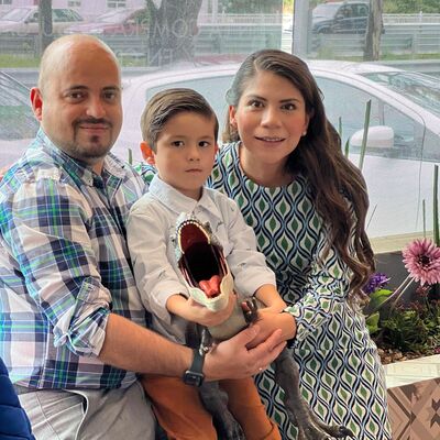 Foto con filtro rosa de una familia formada por una mujer sentada en silla de ruedas y un hombre de pie, ambos dirigiendo una carreola y encima el texto Día Mundial de las Madres y los Padres